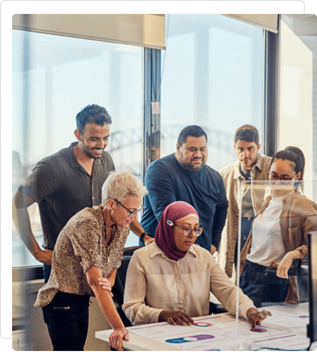 A diverse team collaborates around a computer in a modern office.