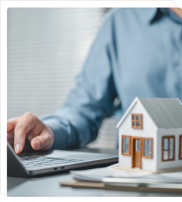 Person using laptop with a small house model on the desk.